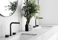 Iron Bronze tapware with tall basin mixers and separate controls on a pale stone double vanity in a bright contemporary bathroom.